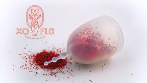zdjęcie reklamowe: przezroczysty kubeczek menstruacyjny wypełniony czerwonym brokatem